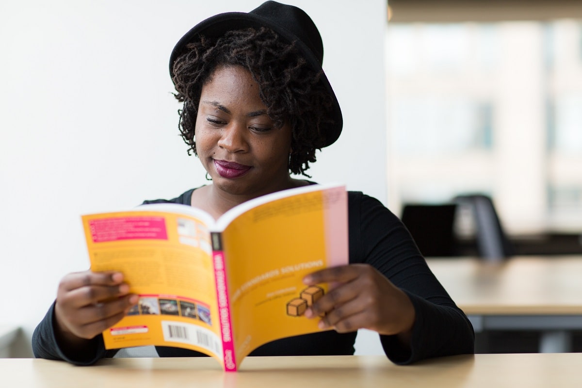 Woman with a hat on reads a colorful book at a white desk